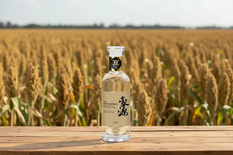 Bottle of The Grand Spring on a wooden surface with a wheat field in the background