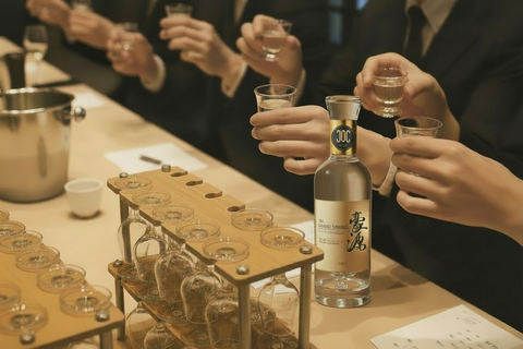 People toasting with glasses at a bar, with a bottle of liquor in the foreground.